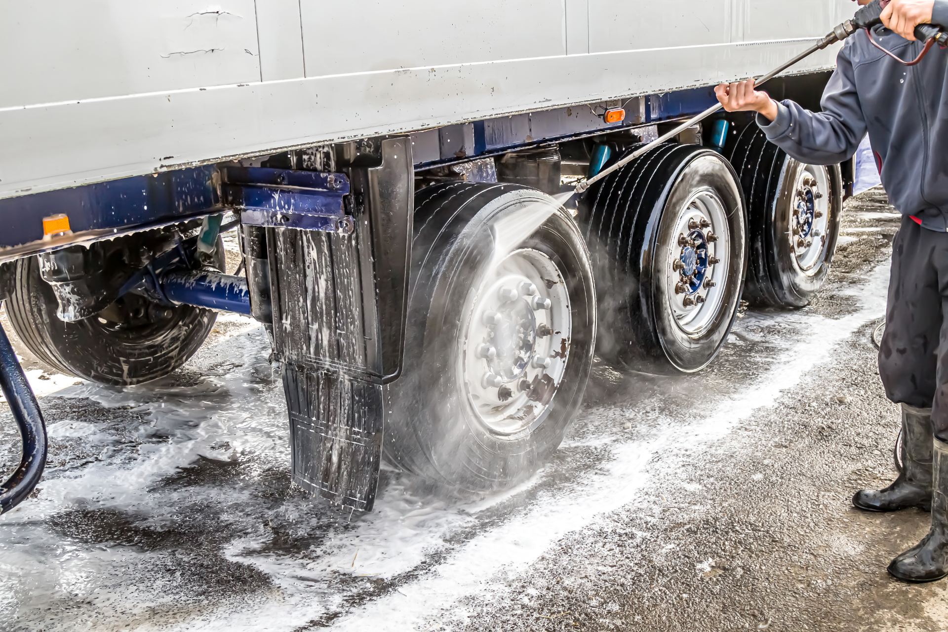 Worker pressure washing truck tires and undercarriage with high-pressure water spray