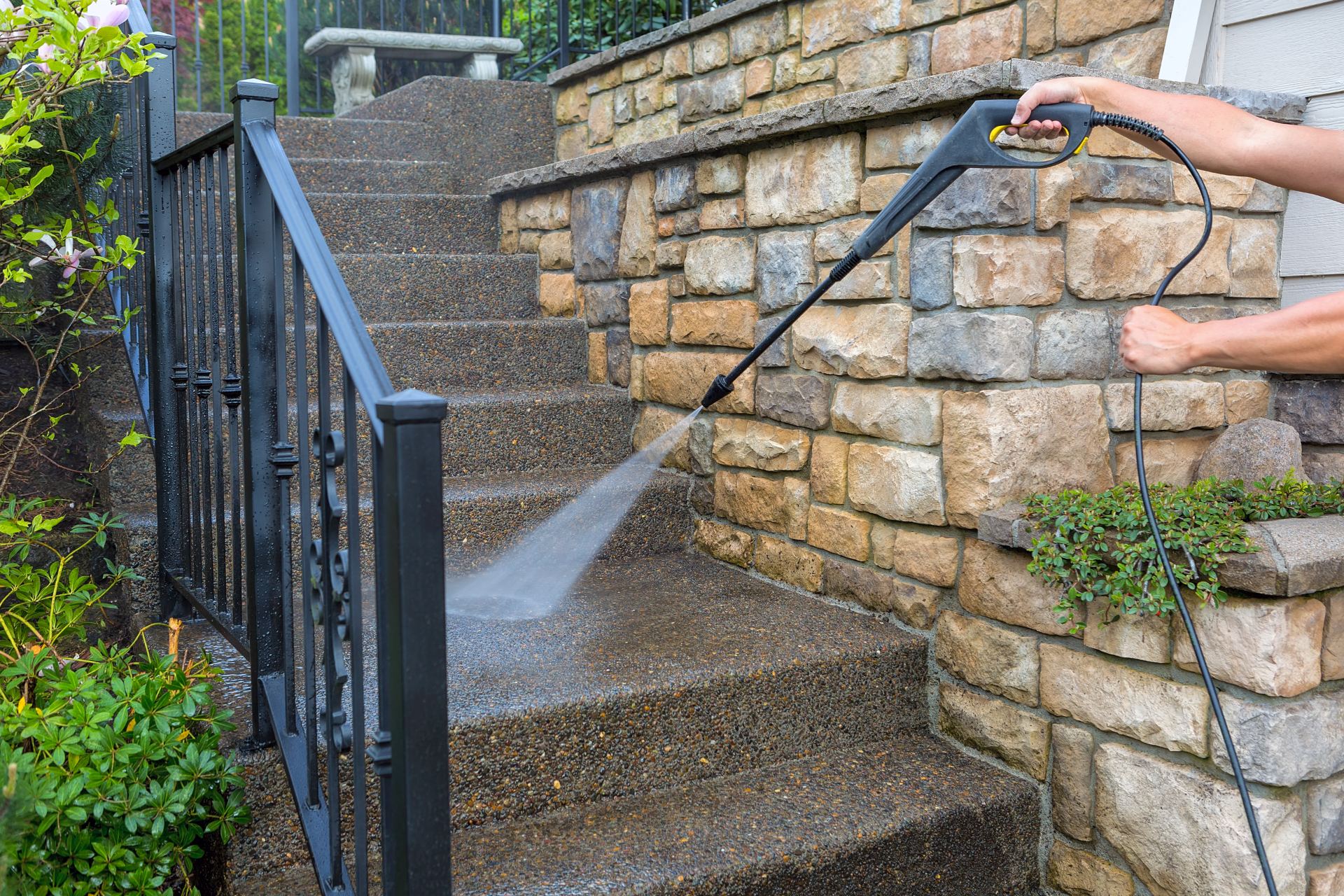 Person using pressure washer to clean stone wall and driveway
