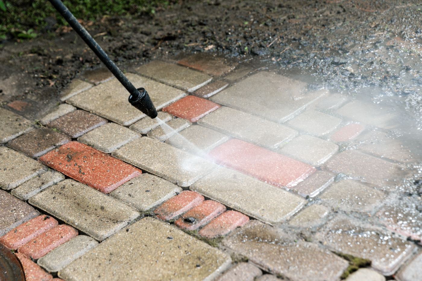 Power washer cleaning brick pavement with water spray